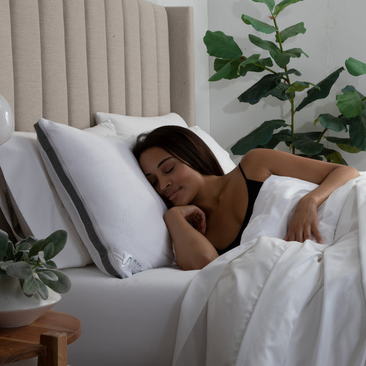 Woman sleeping peacefully in bed with white pillows and a plant in the background