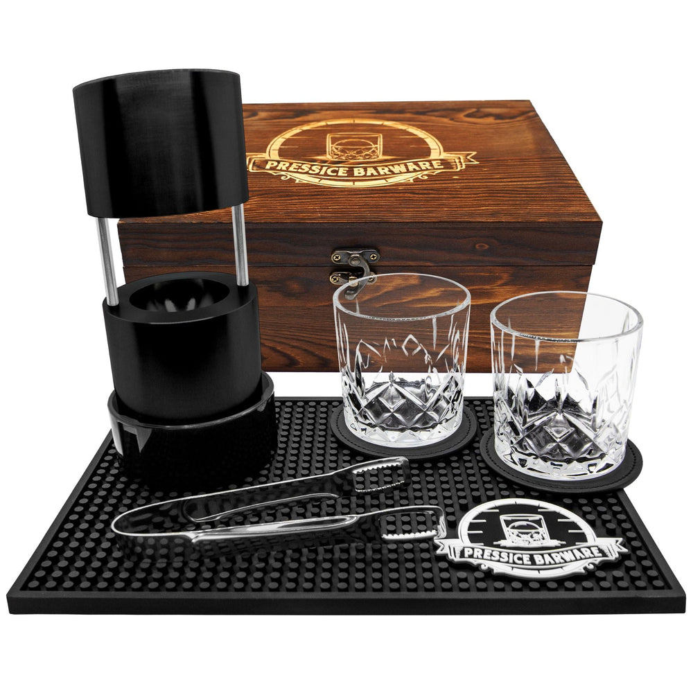 Barware set with two glasses, a black container, and tools on a black mat with a wooden box labeled 'Pressie Barware'.