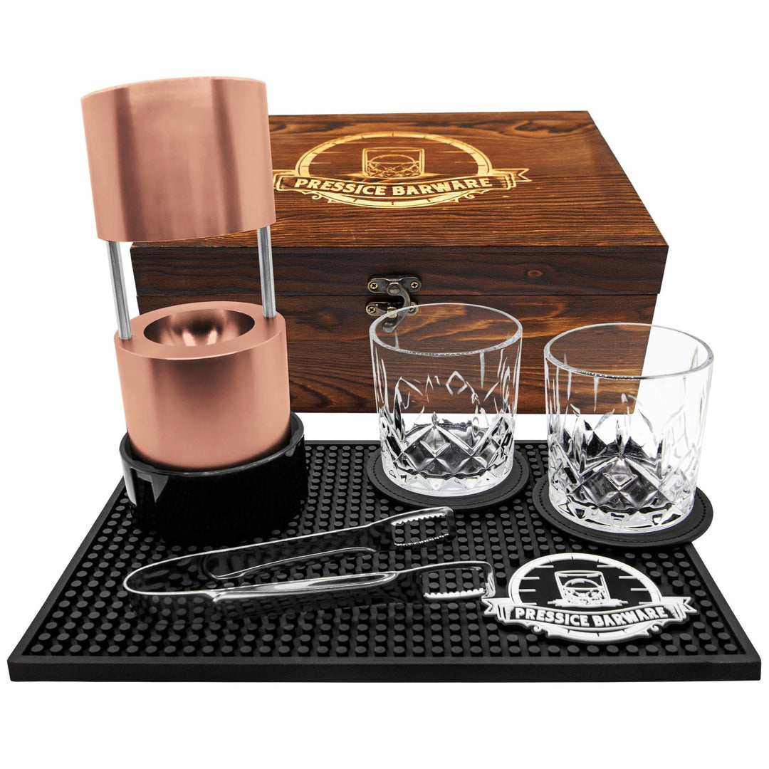 Barware set with copper elements, glasses, and tools on a branded mat and wooden box.