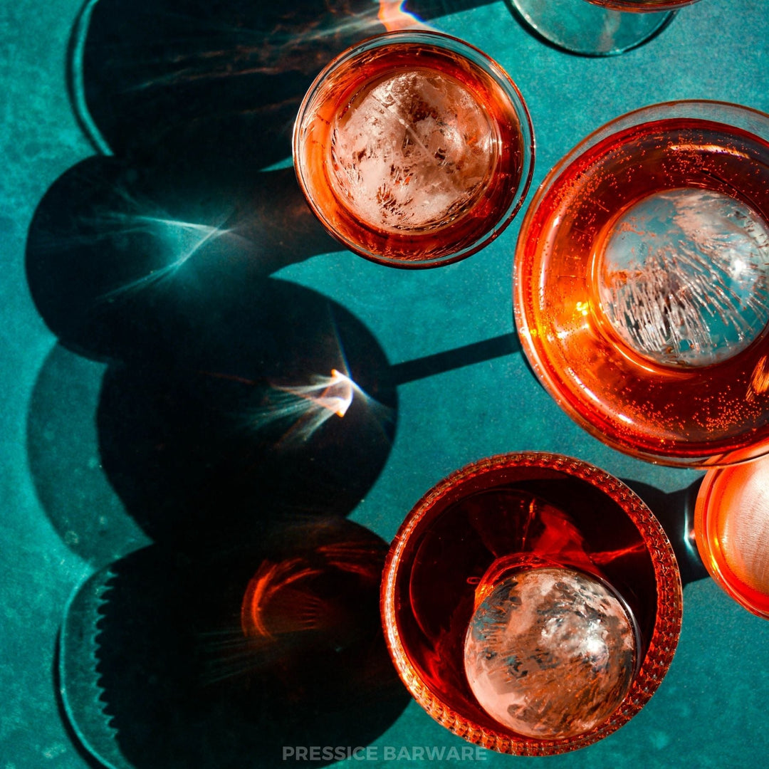 Copper barware with ice cubes on a teal background. Clear ice sphere maker, ice ball press kit by pressice barware.