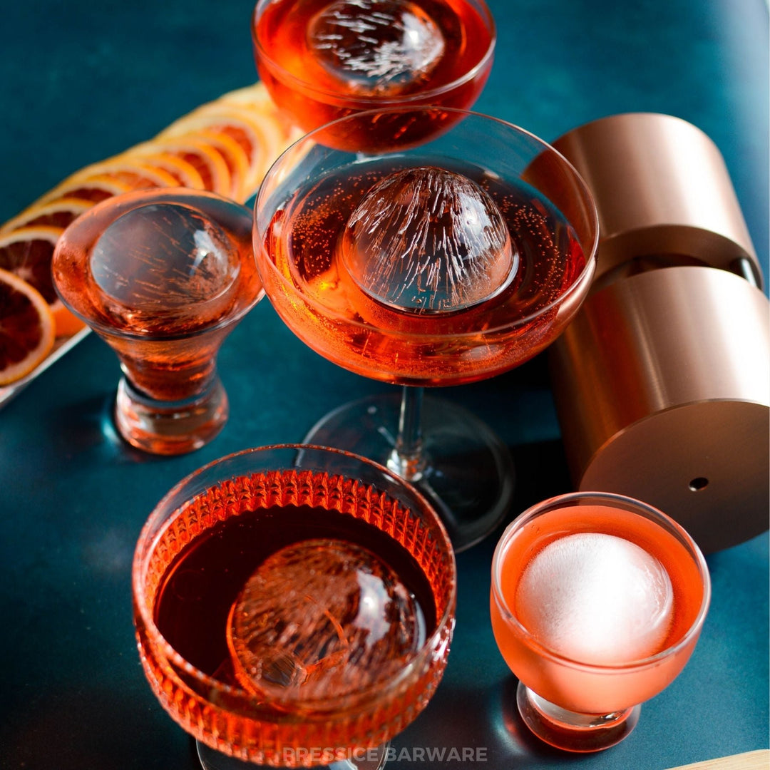 Pressice Barware Ice Ball Press Cocktail glasses with a copper shaker on a blue surface