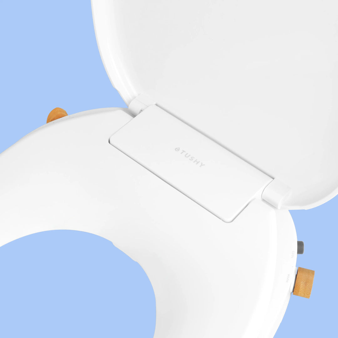 Close up of White TUSHY Oasis bidet seat, with bamboo control knobs, on a blue background