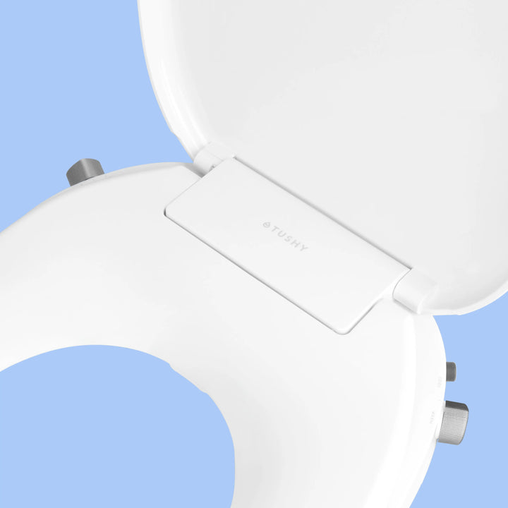 Close up of White TUSHY Oasis bidet seat, with platinum control knobs, on a blue background