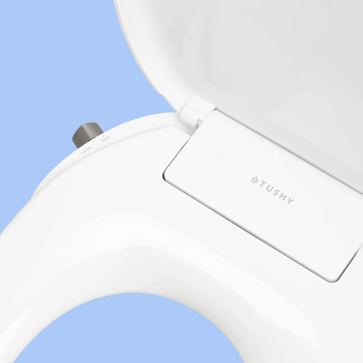 Close up of White TUSHY Oasis bidet seat, with platinum control knob, on a blue background