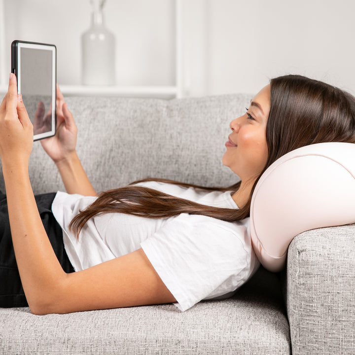 Woman lying on a couch using a tablet with a pillow under her head.