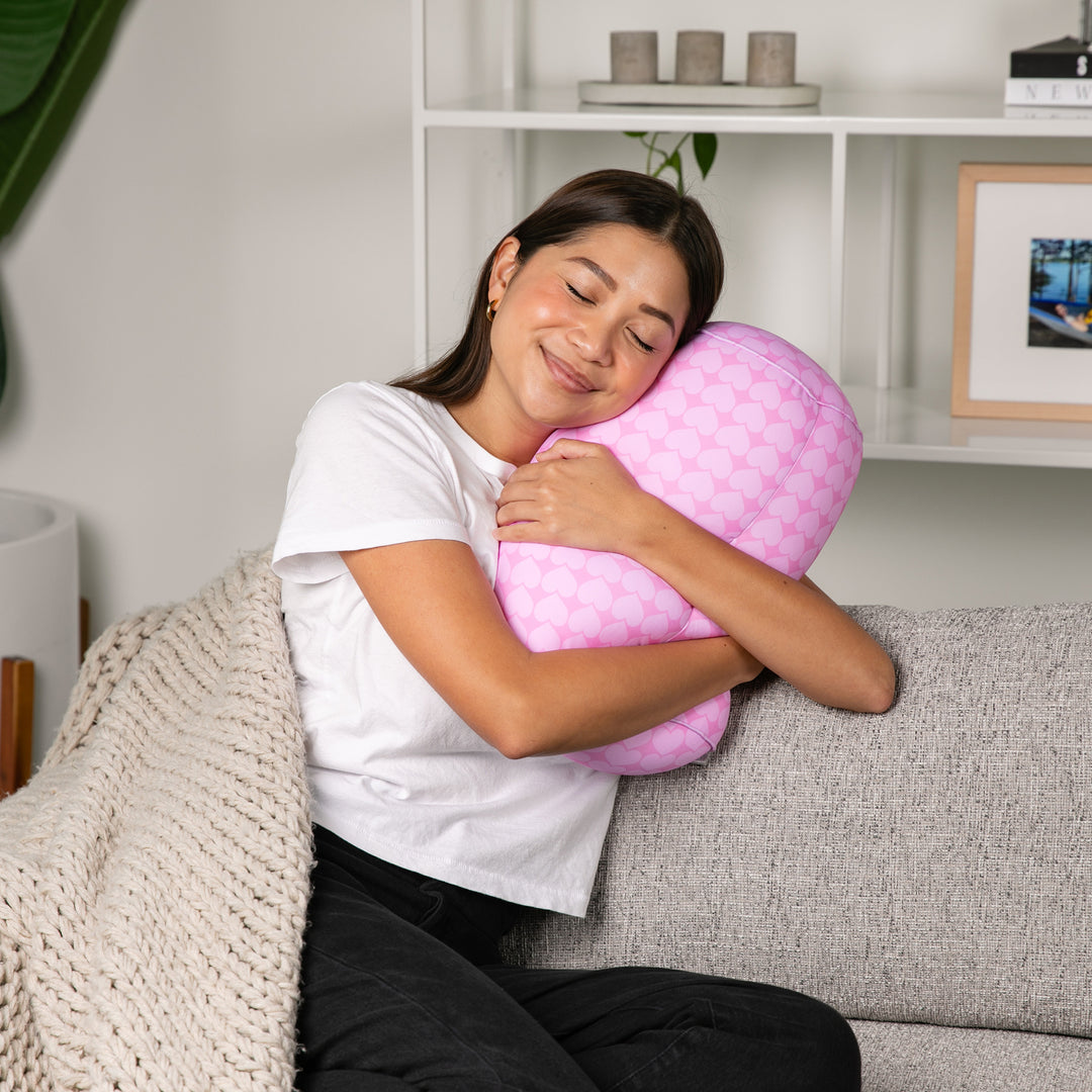 Woman hugging a pink pillow on a couch in a cozy living room.