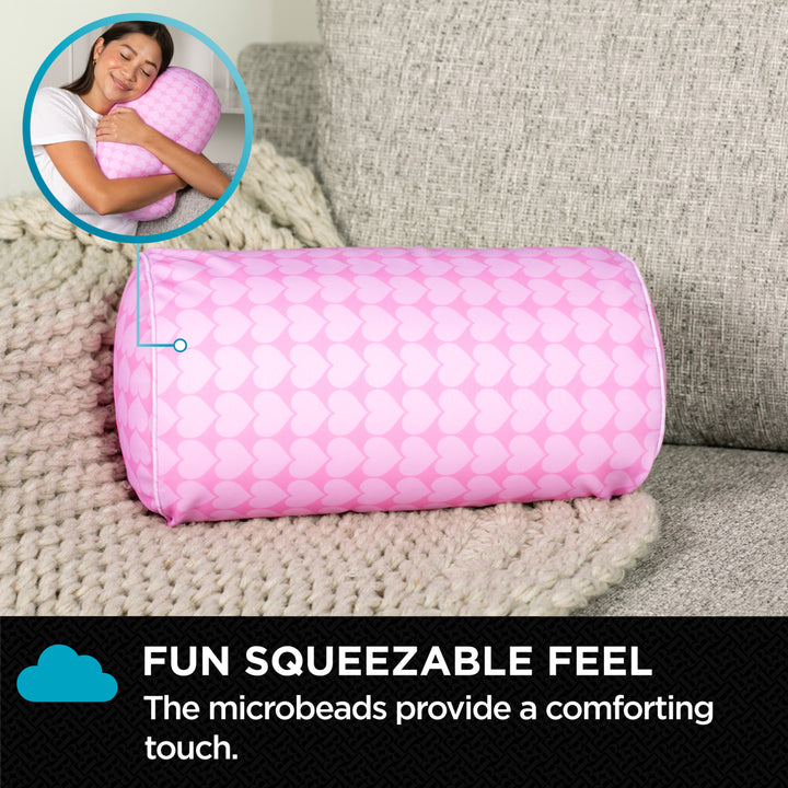 Pink cylindrical pillow with microbeads on a couch, featuring text about its squeezable feel.