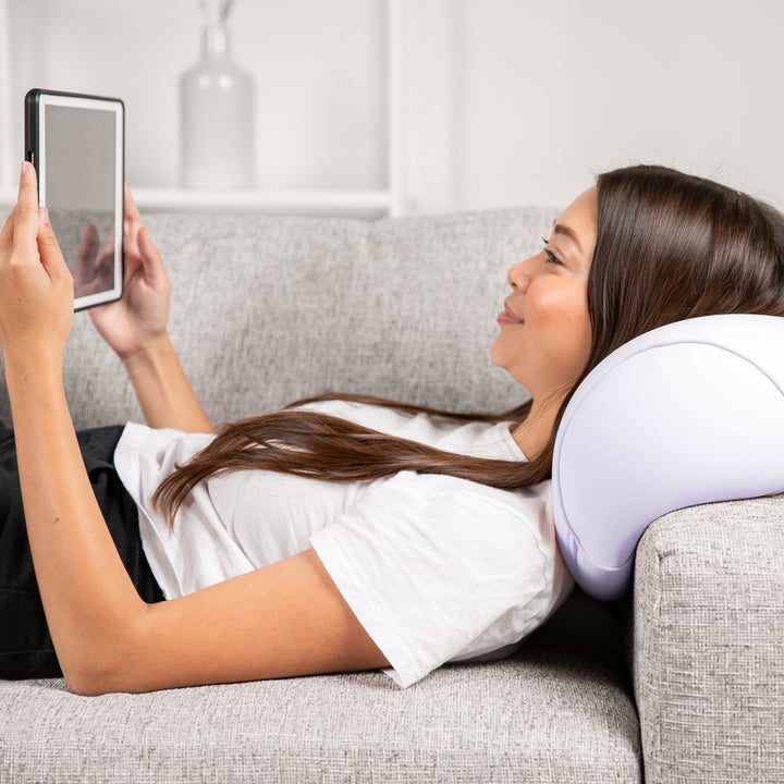Woman using a tablet while lying on a couch with a neck pillow.