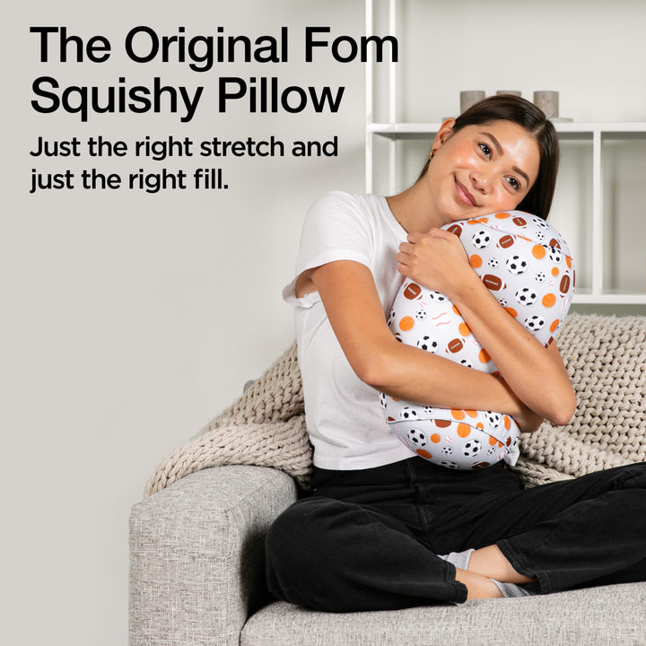 Woman sitting on a couch holding a squishy pillow with text describing it as 'The Original Fom Squishy Pillow'.