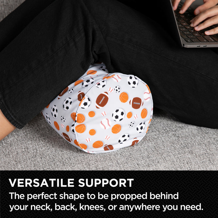 Person using a foot pillow with sports pattern on a gray surface, text 'VERSATILE SUPPORT' below.