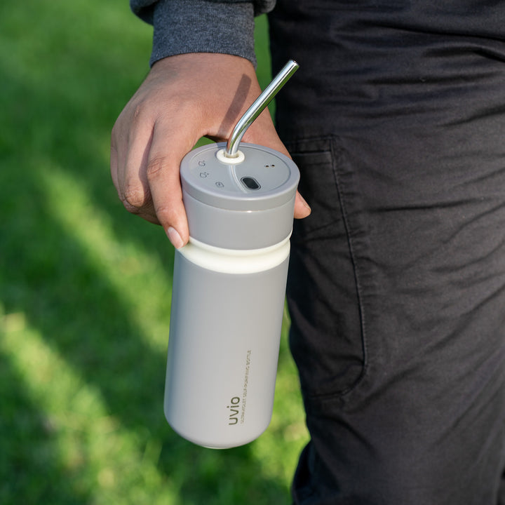 Person holding a gray water bottle with a straw lid outdoors on grass