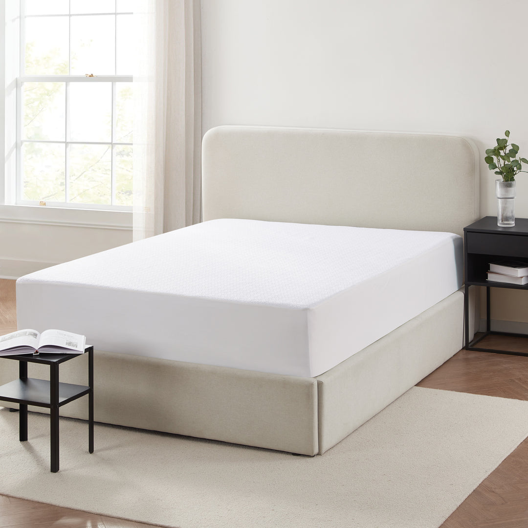Beige bed frame with white mattress in a room with a window and small table.