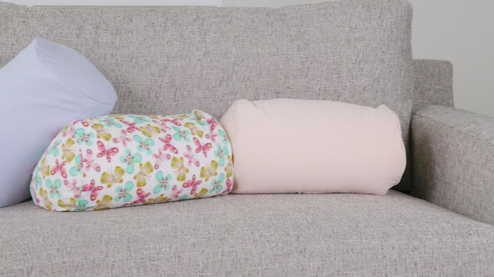 Video showing two cylindrical Fom Fun Cushions on a light gray sofa: one in a pastel butterfly print and the other in a soft apricot solid color.”
