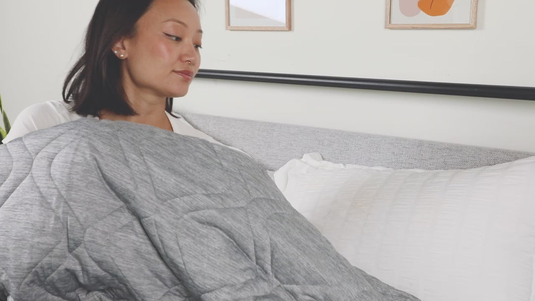 Woman relaxing on a bed while wrapped in a gray cooling comfort throw, demonstrating the blanket’s soft texture and cooling feel.